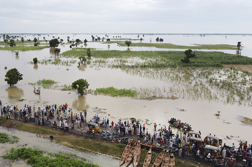 当地时间2022年9月19日，尼日利亚哈德加，暴雨引发洪水，农田被淹没，人们在积水道路上通行。