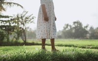 woman in white and pink floral dress standing on green grass field during daytime 白天，穿白色和粉色花裙的女人站在绿草地上。