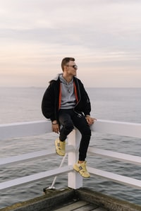 man in black jacket and black pants wearing yellow nike sneakers standing on gray sand during 身穿黑色夹克和黑色裤子的男子穿着黄色耐克运动鞋，站在灰色的沙滩上