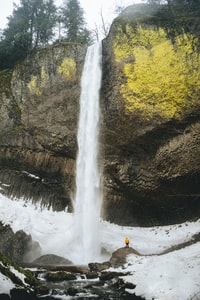 person in orange jacket standing on rock near waterfalls during daytime 白天穿着橙色夹克站在瀑布附近岩石上的人