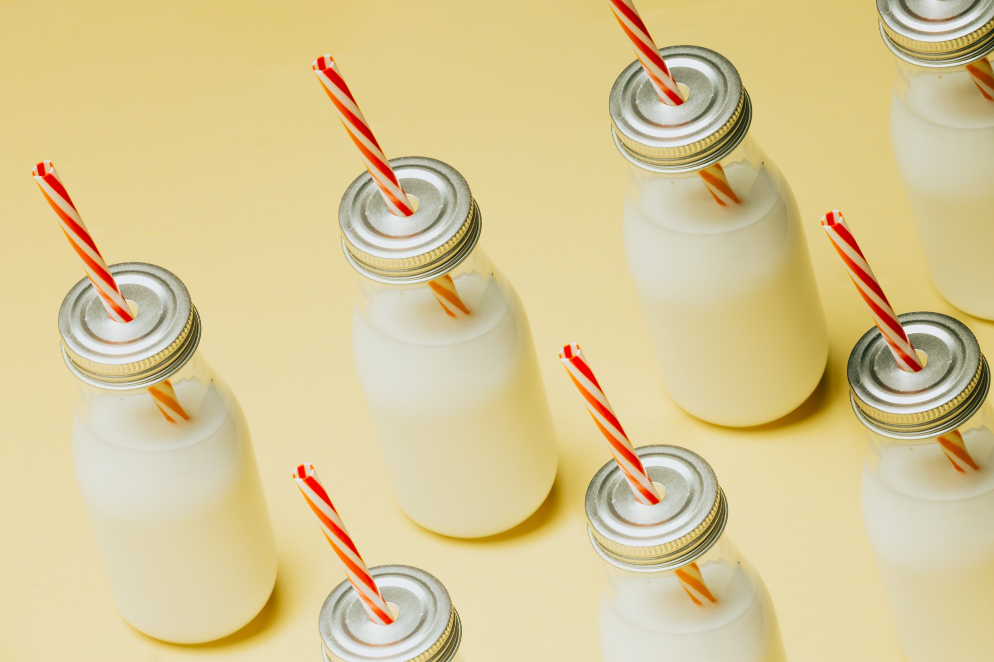 milk bottles with red striped straws on a yellow surface 黄色表面有红色条纹吸管的奶瓶
