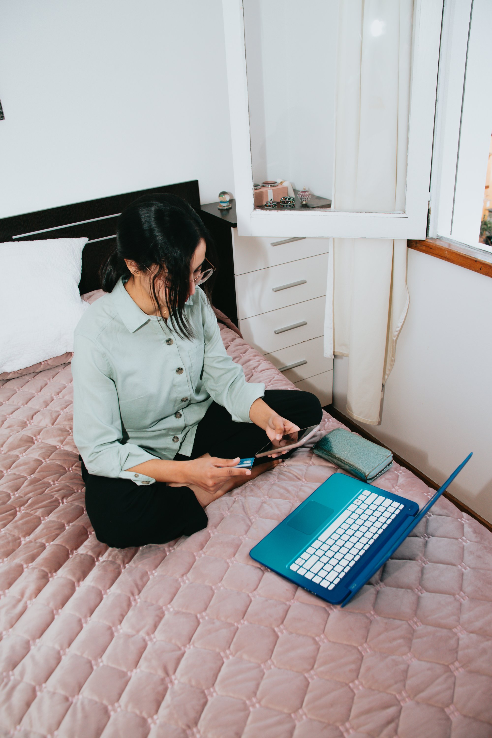 woman sitting on pink bed with her laptop and pphone 女人坐在粉红色的床上，手里拿着笔记本电脑和电话机。