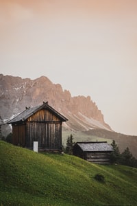 brown wooden house on green grass field near brown mountain during daytime 白天，棕色山附近绿草地上的棕色木屋