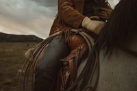 woman in brown leather jacket riding white horse during daytime 白天穿棕色皮夹克骑白马的女人
