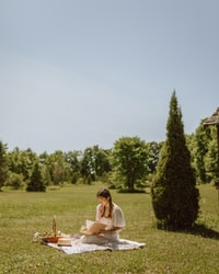 woman in white dress sitting on green grass field during daytime 白天穿着白色连衣裙坐在绿草地上的女人