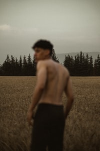 topless man in black shorts standing on brown grass field during daytime 白天，穿着黑色短裤的无上身男子站在棕色草地上。