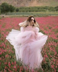 woman in white dress sitting on red flower field during daytime 白衣女人白天坐在红花坛上