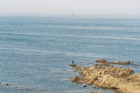 person standing on rock formation in front of body of water during daytime 白天站在水面前的岩层上的人