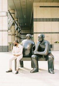 man in white suit standing beside black statue 身穿白色西服的男子站在黑雕像旁边
