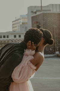 man in black suit kissing woman in pink dress during daytime 白天穿黑色西服的男人亲吻穿粉红色衣服的女人