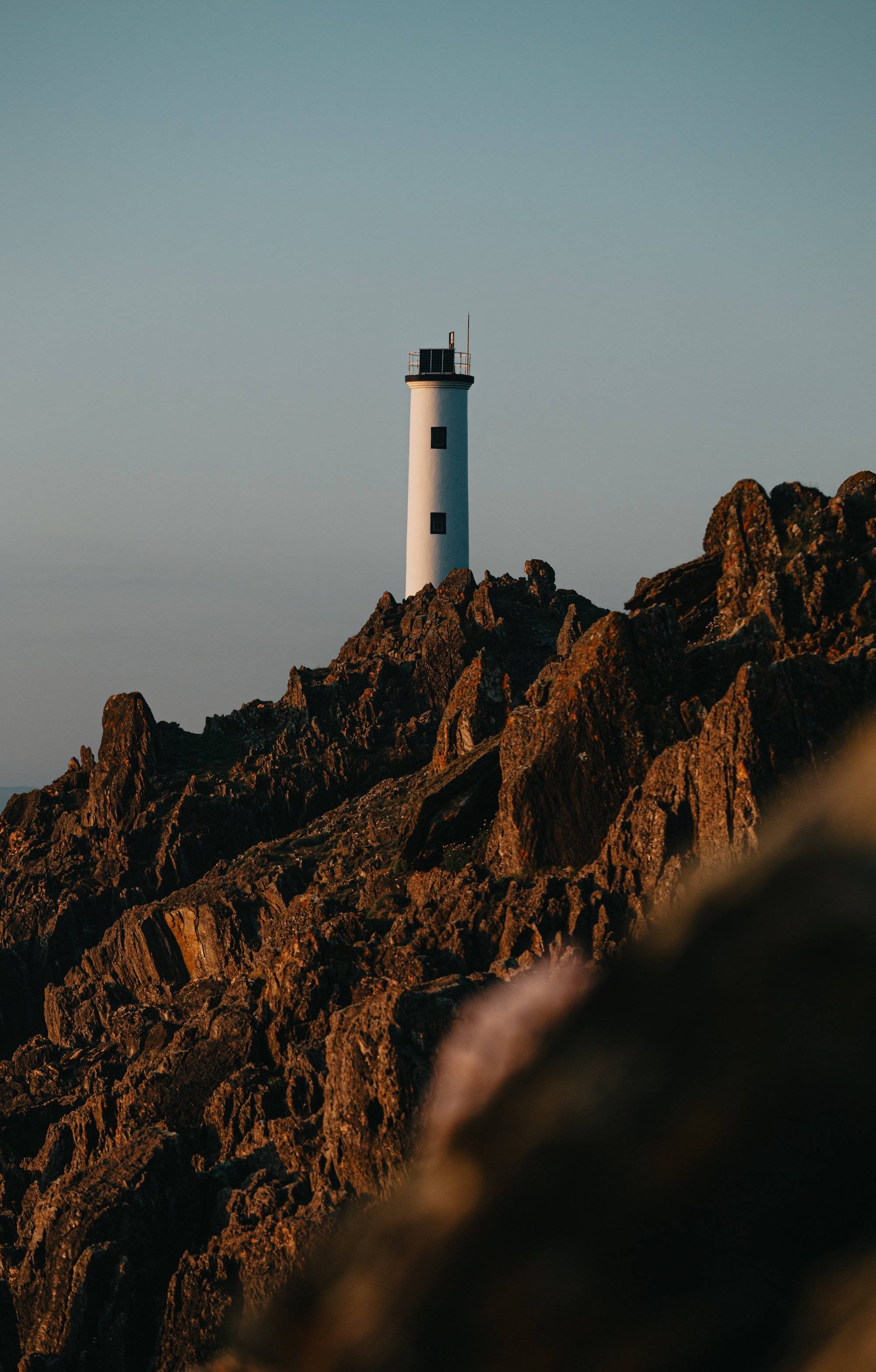 a lighthouse sits on top of a sharp mountain ridge 一座灯塔坐落在一座陡峭的山脊上。