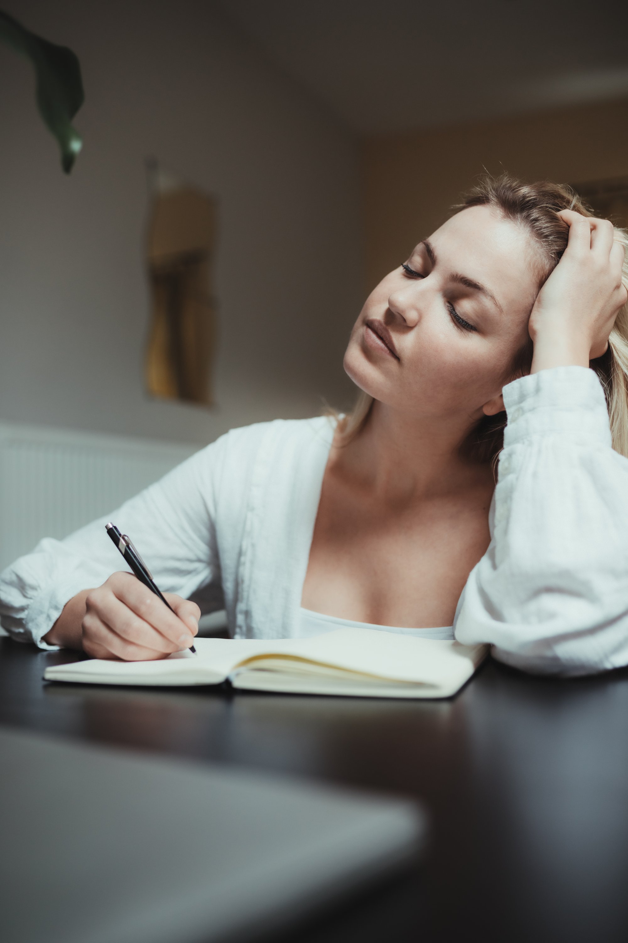 woman holds her head thinking while writing in a journal 在日记里写作时，女人抱着头思考。