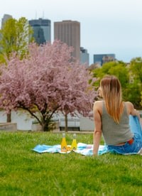 woman in gray tank top and blue denim shorts sitting on green grass field during daytime 白天穿着灰色背心和蓝色牛仔短裤坐在绿草地上的女人