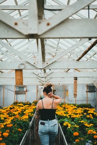 woman in black spaghetti strap top standing on yellow flower field during daytime 白天穿着黑色意大利面带子的女人站在黄色的花坛上。
