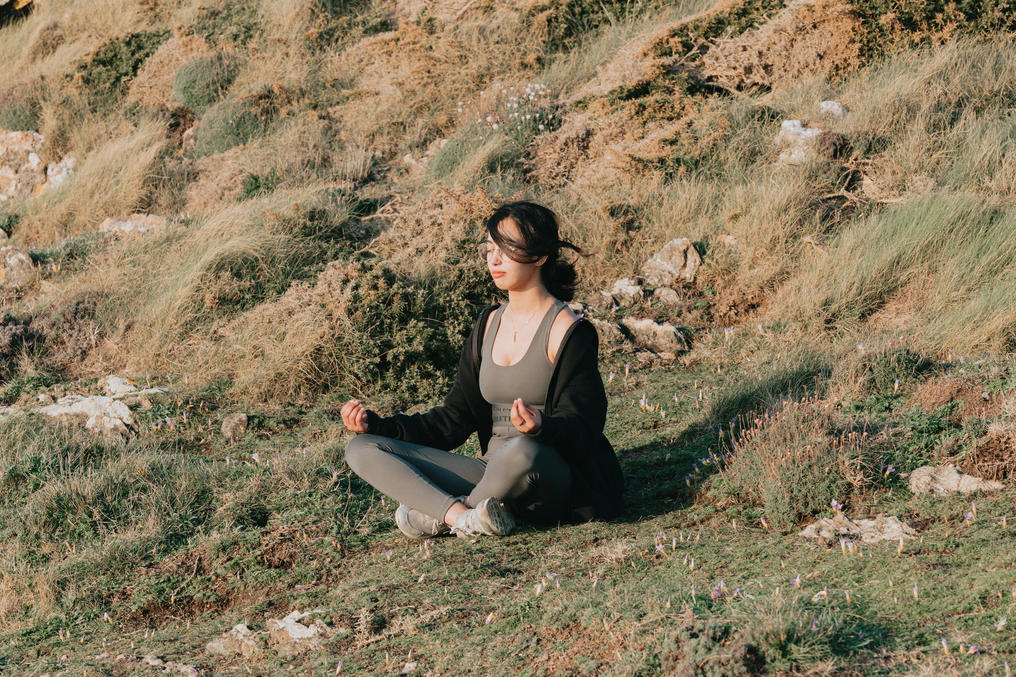 woman meditates outdoors on a green grassy hill 女人在绿色的长满草的小山上打坐。