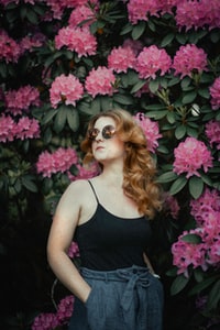 woman in black tank top wearing sunglasses standing beside pink flowers 身穿黑色背心的女子戴着太阳镜站在粉红色的花朵旁边。
