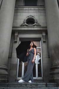 woman in black and white stripe dress covering her face with black umbrella standing on gray