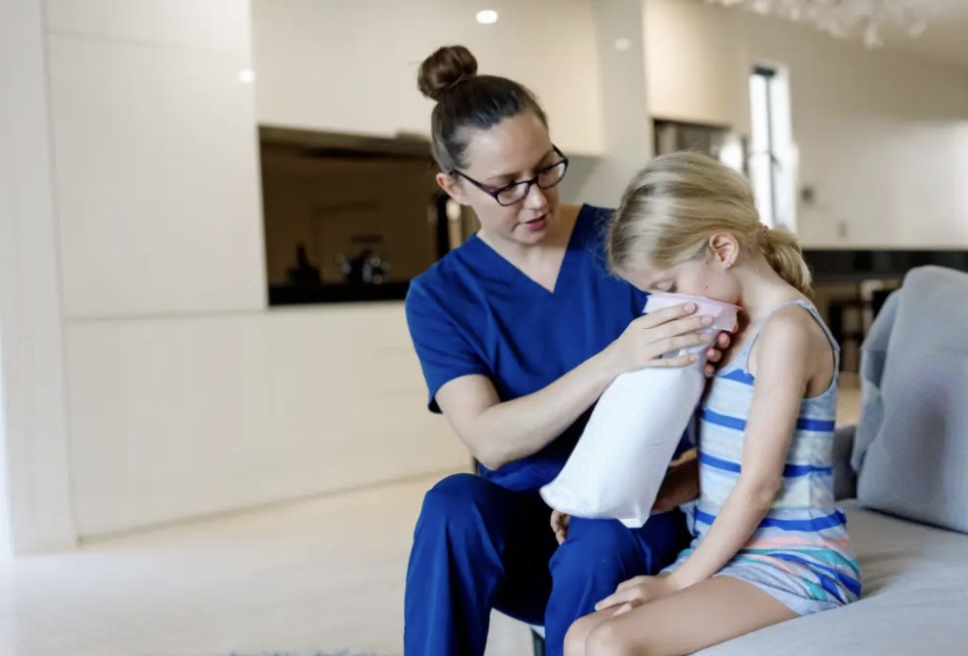 A healthcare provider holds a disposable vomit bag steadily for the young blonde girl beside her and helps her carefully. A healthcare provider holds a disposable vomit bag steadily for the young blonde girl beside her and helps her carefully.
