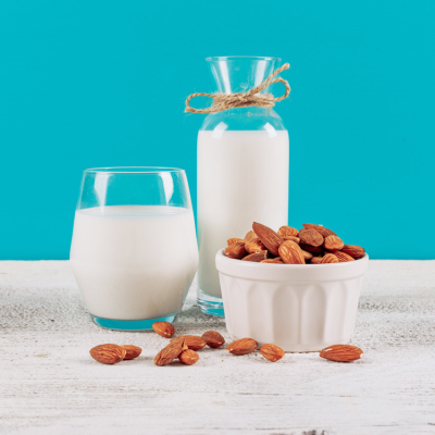 Bottle of milk with glass of milk and bowl of almonds side view